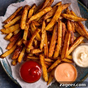 Crispy Homemade Oven Chips Recipe: Perfectly Golden Fries 7 Chips on a plate on top of baking parchment. 3 dipping bowls of sauce on the plate.