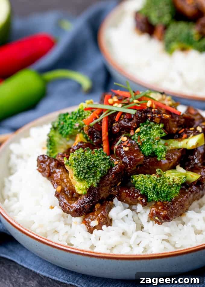 Crispy Tangy Beef with Broccoli in Sweet Glaze 2 Crispy beef strips and broccoli in a tangy sauce on top of a bowl of boiled rice. Further bowl in the background.