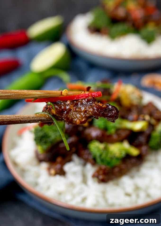 Crispy Tangy Beef with Broccoli in Sweet Glaze 4 Chopsticks taking a piece of beef from a bowl of crispy beef and broccoli with rice