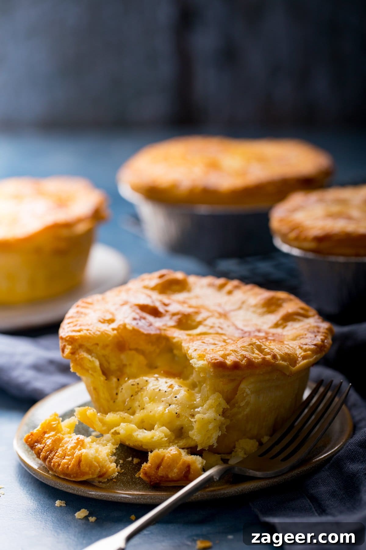Chip Shop-Style Individual Cheese and Onion Pies 7 4 individual cheese and onion pies on a blue surface. Piece taken out of the pie at the front of the image.