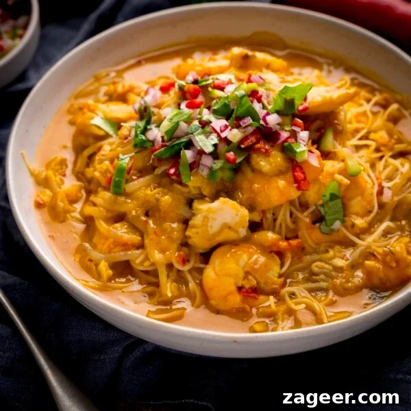 20-Minute Chorizo and Butterbean Soup Recipe 11 Square image of seafood laksa in a white bowl on a dark surface. The laksa is topped with a coriander-chilli-red onion garnish.