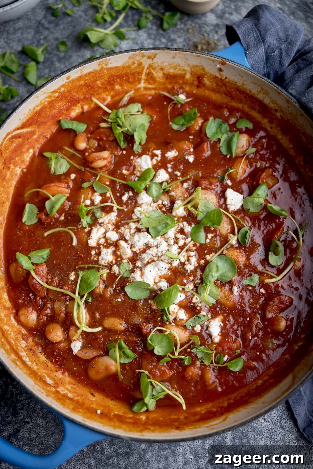 20-Minute Chorizo and Butterbean Soup Recipe 4 Overhead image of a blue cast iron pan filled with butterbean and chorizo soup. The pan on on a grey background.
