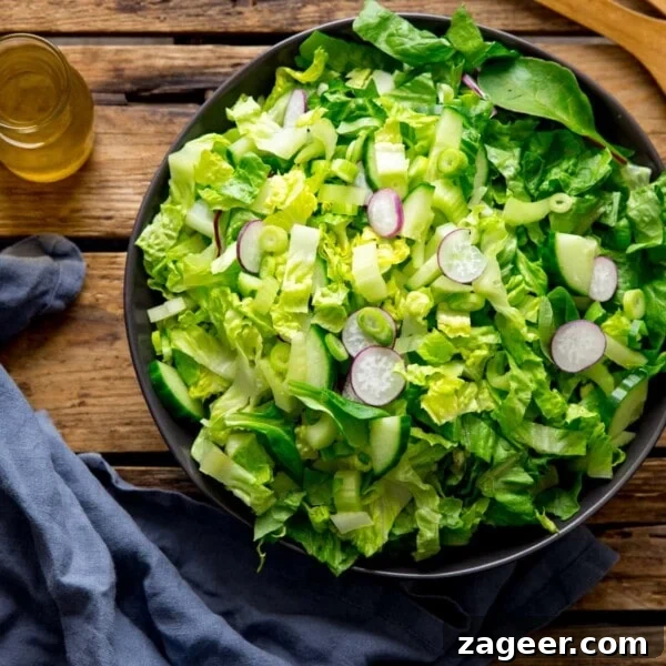 20-Minute Chorizo and Butterbean Soup Recipe 5 Large bowl of green salad on a wooden surface. Blue napkin and jar of salad dressing is next to the bowl.