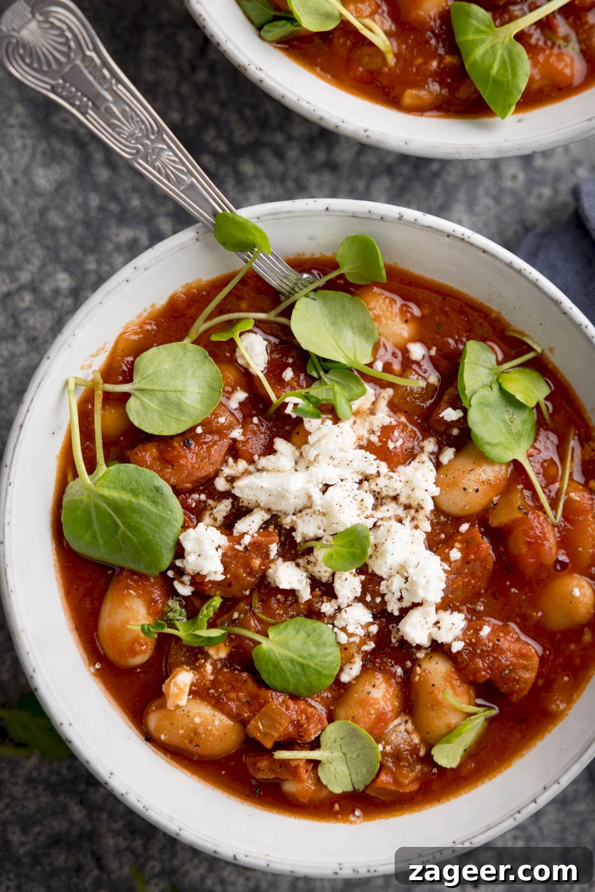20-Minute Chorizo and Butterbean Soup Recipe 8 Overhead of butterbean and chorizo soup topped with feta and watercress in a light bowl. There is a second bowl just in shot at the top of the frame.