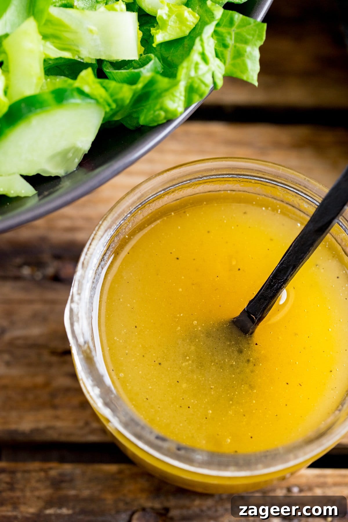 Homemade Honey Mustard Dressing Recipe 3 Overhead shot of a jar of honey mustard salad dressing on a wooden table. Bowl of salad partially in shot.