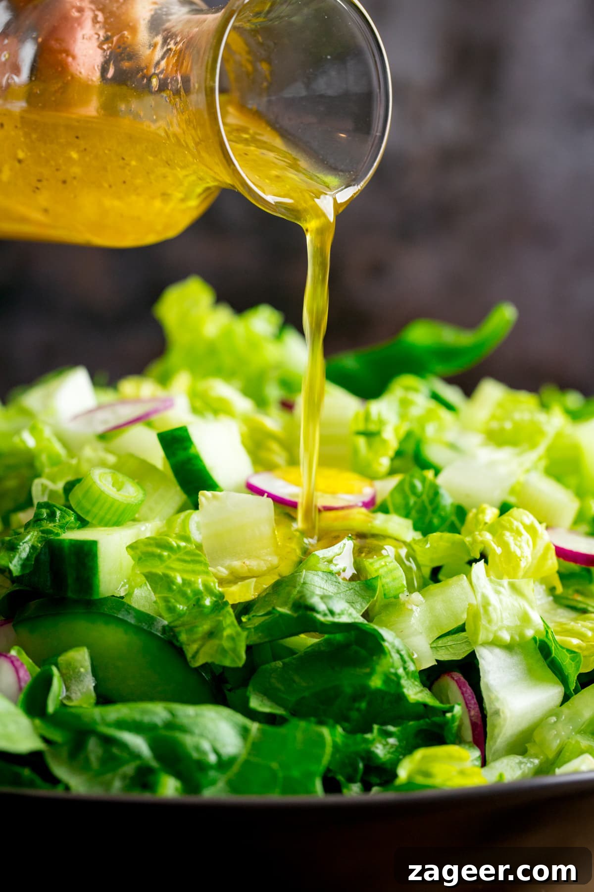 Crisp Green Salad with Tangy Vinaigrette Dressing 2 Vinaigrette dressing being poured from a small glass jar onto a green salad.