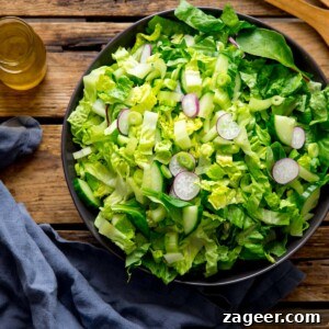 Crisp Green Salad with Tangy Vinaigrette Dressing 10 Large bowl of green salad on a wooden surface. Blue napkin and jar of salad dressing is next to the bowl.