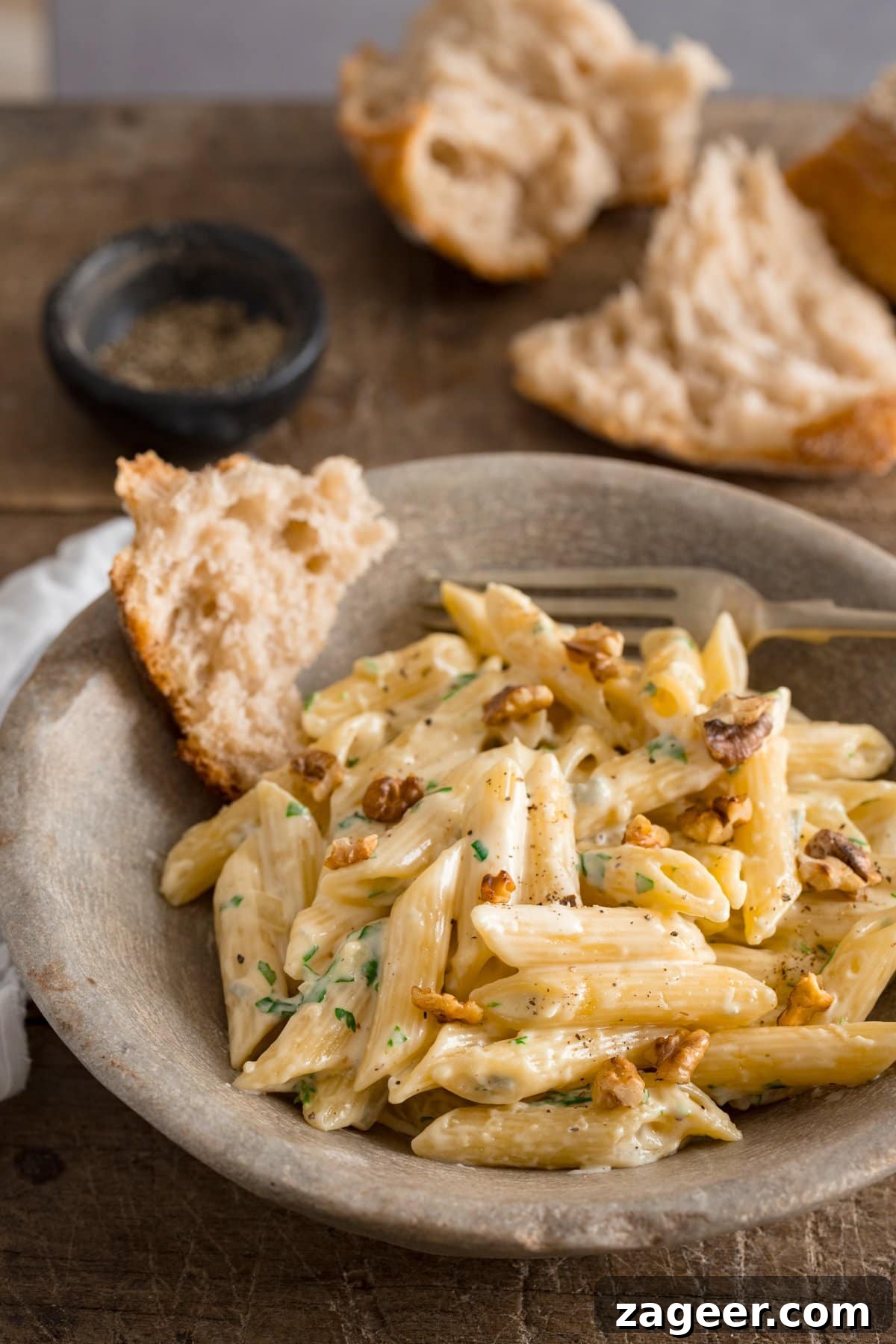 Creamy Gorgonzola Pasta with Garlic and Walnut Crumble 2 Gorgonzola pasta in a stone bowl on a wooden table. Pieces of bread in the bowl and in the background.