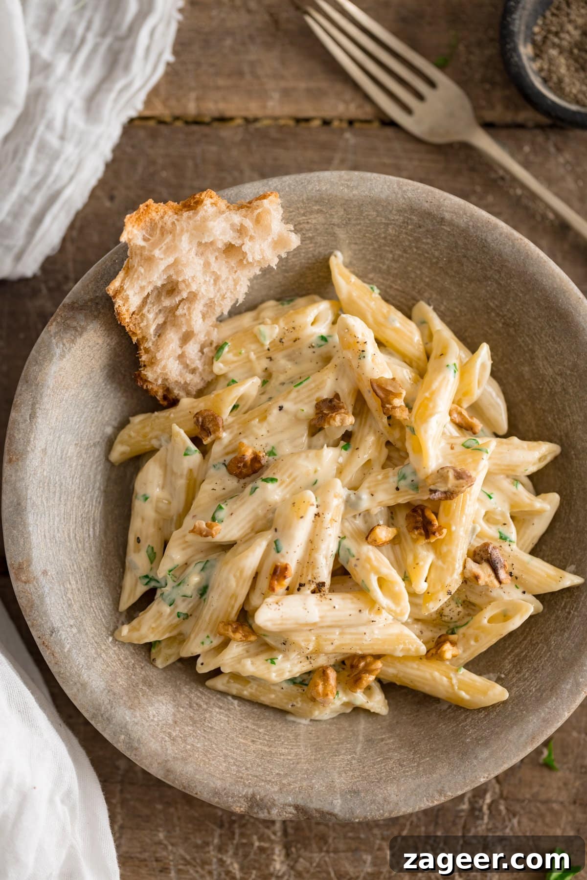 Creamy Gorgonzola Pasta with Garlic and Walnut Crumble 6 Overhead image of gorgonzola pasta in a stone bowl on a wooden table. There is a chunk of bread in the bowl with the pasta.