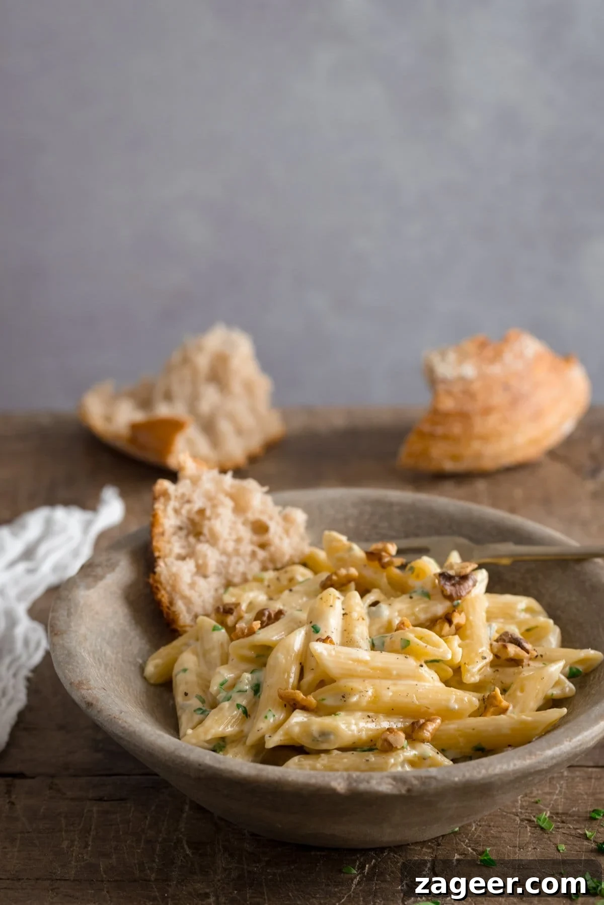 Creamy Gorgonzola Pasta with Garlic and Walnut Crumble 7 Stone bowl filled with gorgonzola penne pasta on a wooden table against a light grey background.