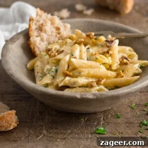 Creamy Gorgonzola Pasta with Garlic and Walnut Crumble 8 Square image of gorgonzola pasta in a light grey bowl on a wooden table. There is a piece of torn bread in the bowl with the pasta.