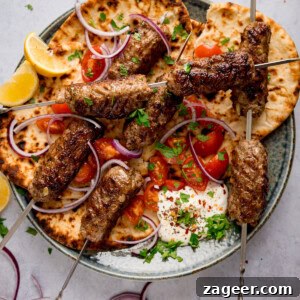 Authentic Lamb Kofta Recipe with Tangy Yogurt Sauce 6 Grilled lamb kofta skewers on flatbread with sliced red onions, cherry tomatoes, lemon wedges, fresh herbs, and a dollop of whipped feta on a plate.