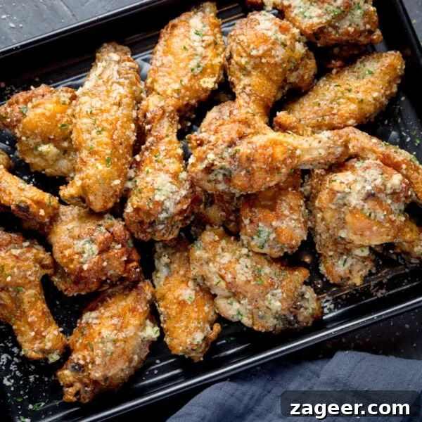 Sichuan Bang Bang Chicken Salad Recipe: Spicy Sesame Chicken 10 A square, overhead shot of a pile of Garlic Parmesan Chicken Wings on a black rectangular baking tray. In the bottom right corner of the image, you can see a dark grey napkin tucked beneath the tray. This is all set on a dark grey background.