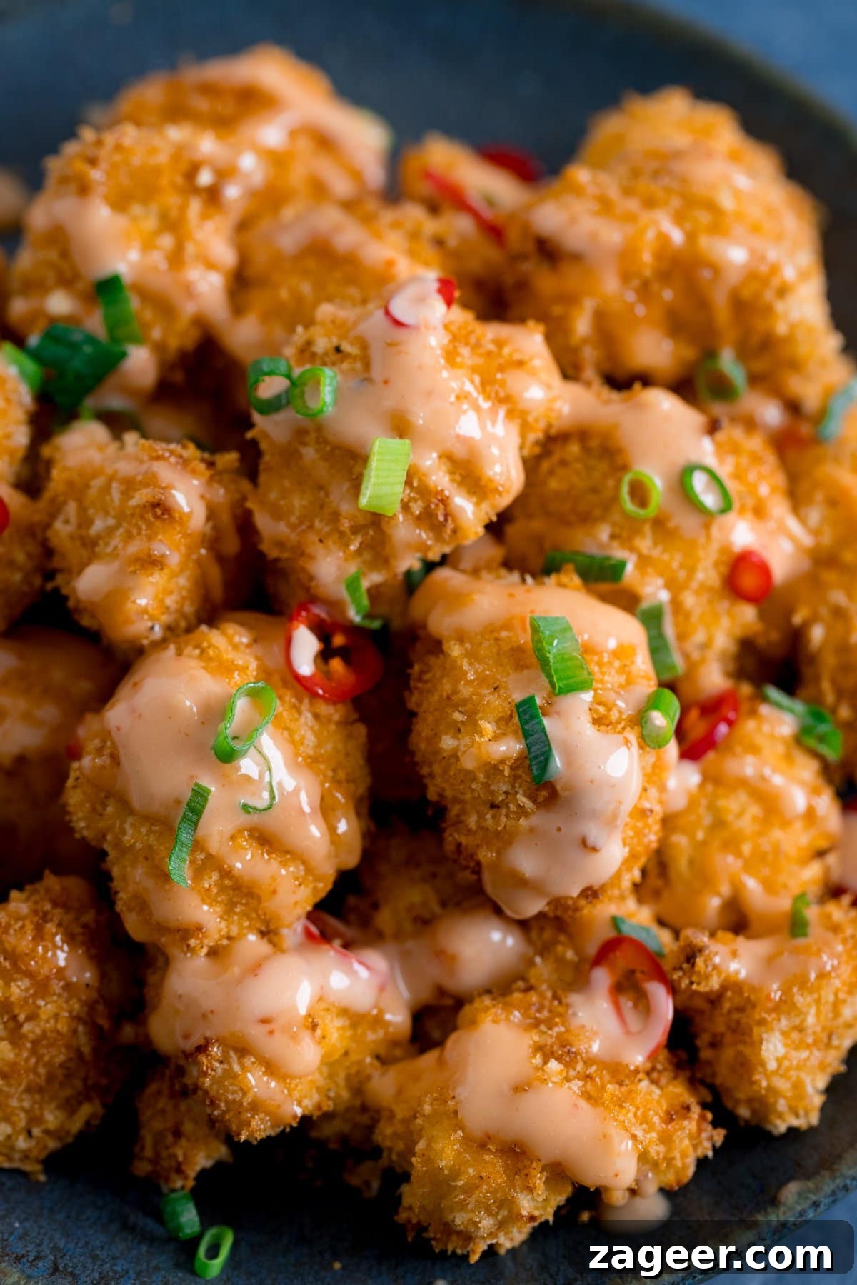 Crispy Bang Bang Cauliflower with Spicy Creamy Sauce 2 Close up of Crispy Cauliflower with bang bang sauce on a dark plate, topped with chillies and spring onions