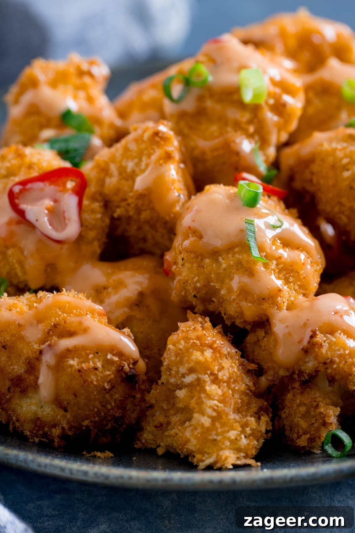 Crispy Bang Bang Cauliflower with Spicy Creamy Sauce 4 Bang bang cauliflower with chillies and spring onions on a dark plate.