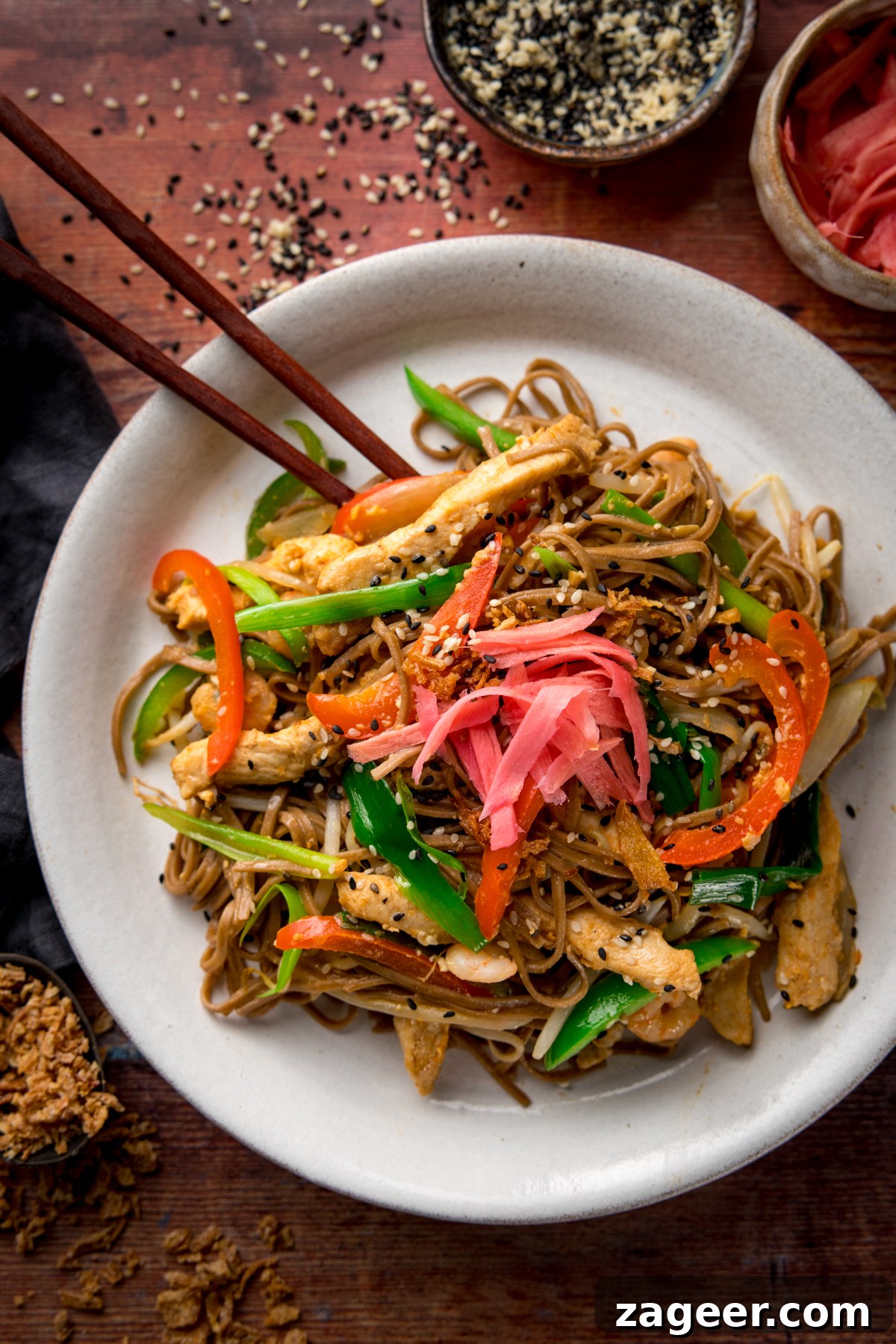Chicken Yakisoba Recipe: Flavorful Stir-Fried Noodles with Veggies 4 A tall image of chicken yakisoba on a white plate with some chopsticks, on a wooden board