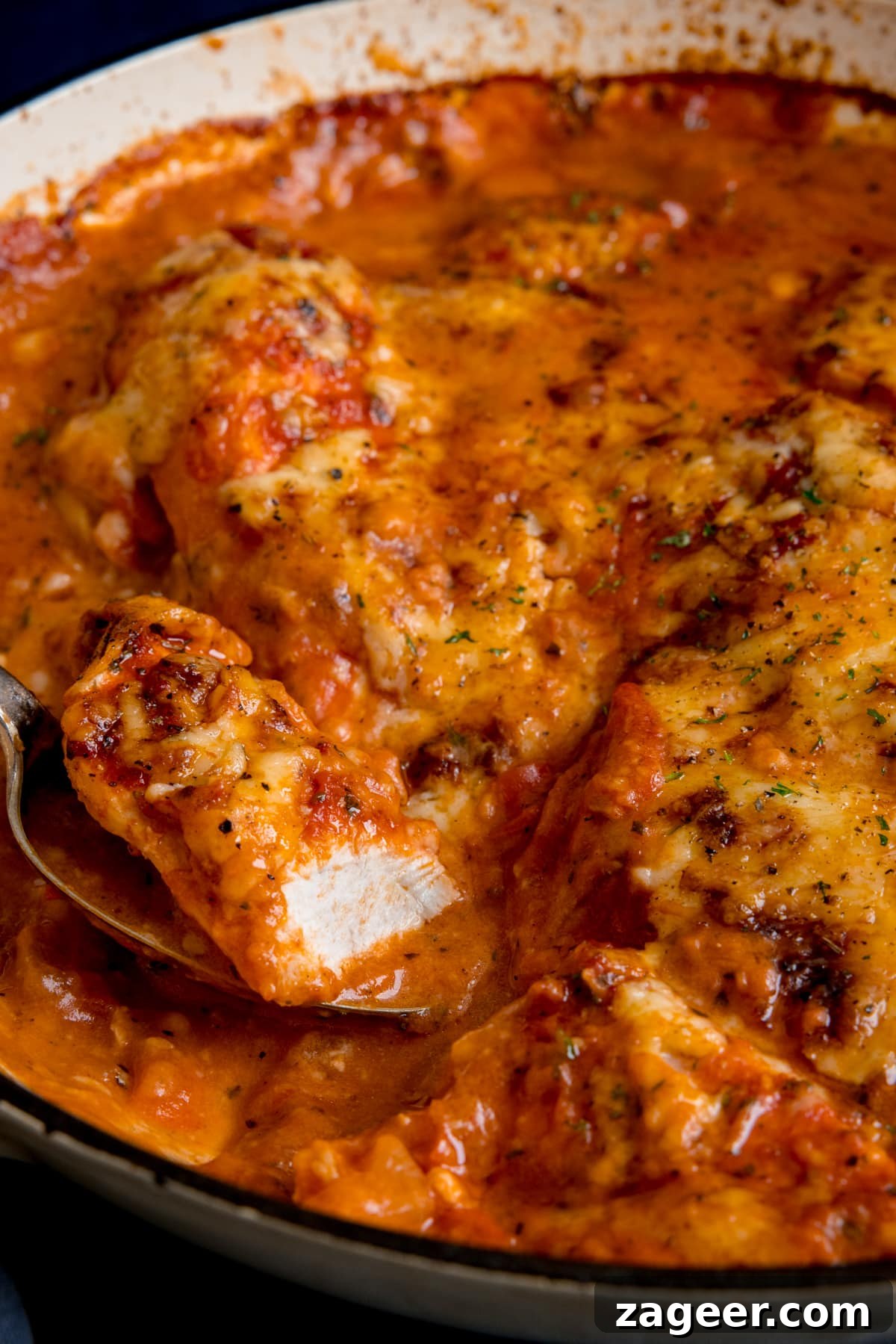 Lasagna-Style Baked Chicken Casserole Recipe 2 Lasagne style chicken bake in a large cast iron pan. A spoonful of chicken is being taken from the pan.