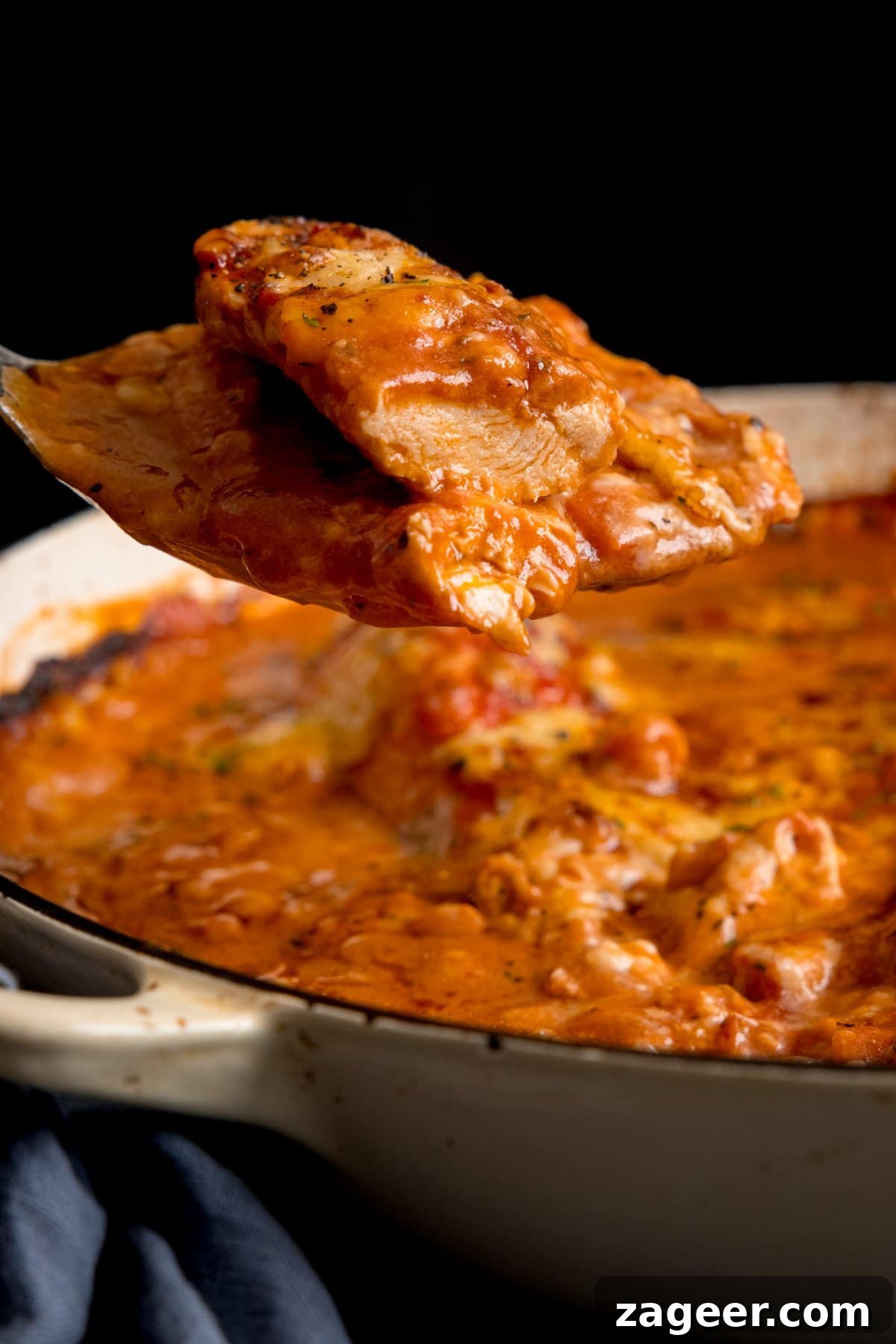 Lasagna-Style Baked Chicken Casserole Recipe 5 Side image of a spoonful of chicken being lifted from a pan of chicken tomato bake.