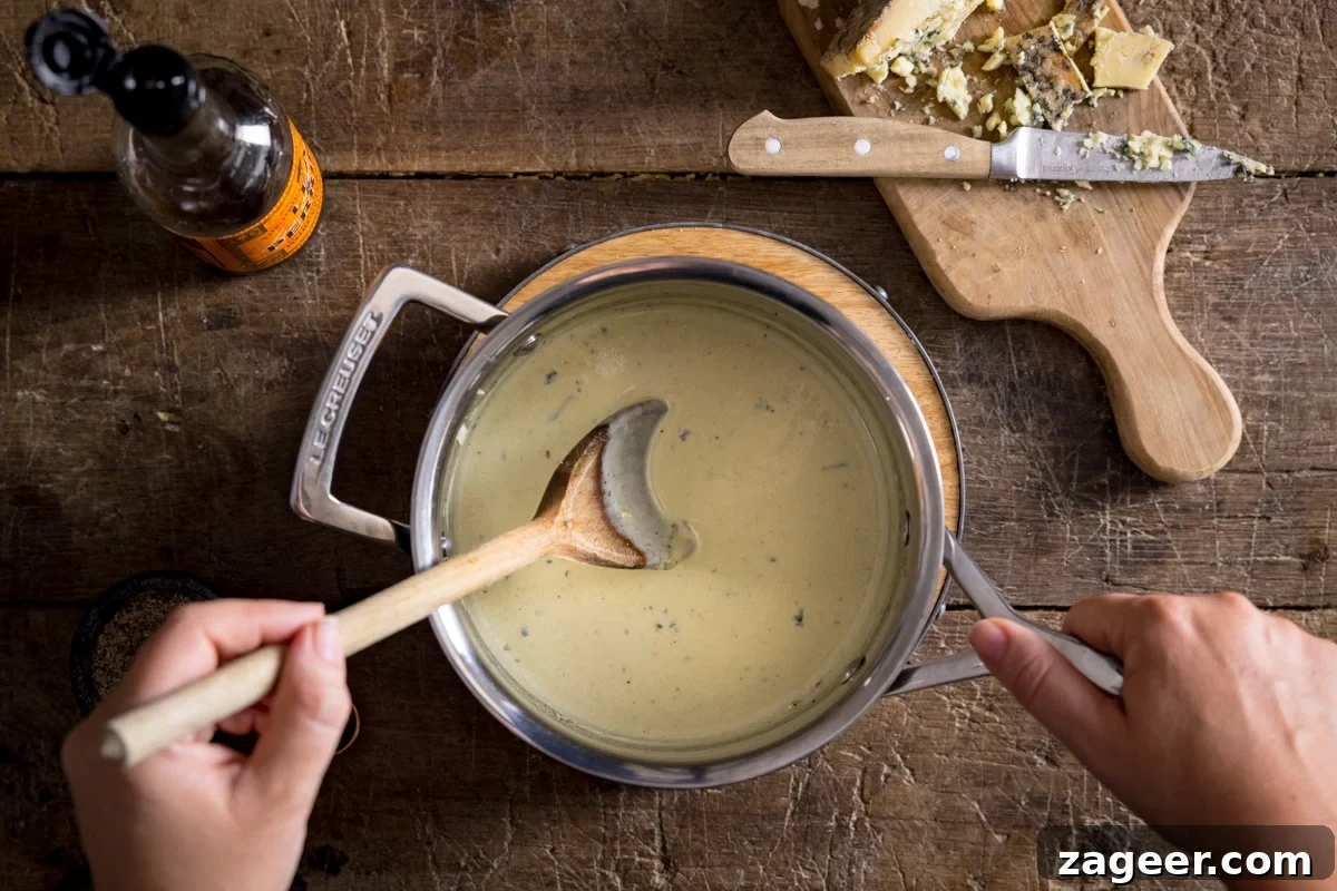 Creamy Blue Cheese Sauce Recipe for Steak and Wings 4 A pan of blue cheese sauce being stirred with a wooden spoon