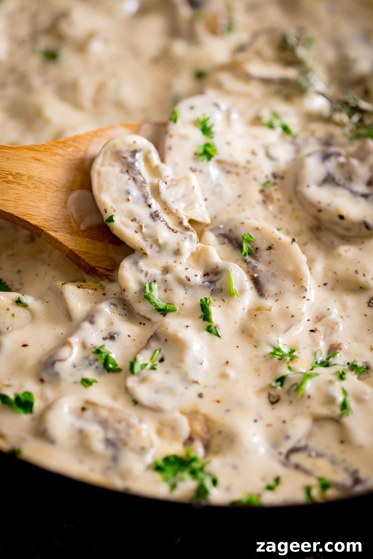 Creamy Mushroom Sauce Recipe for Pasta, Steak & Chicken 2 A tall image of creamy mushroom sauce with a wooden spoon in it