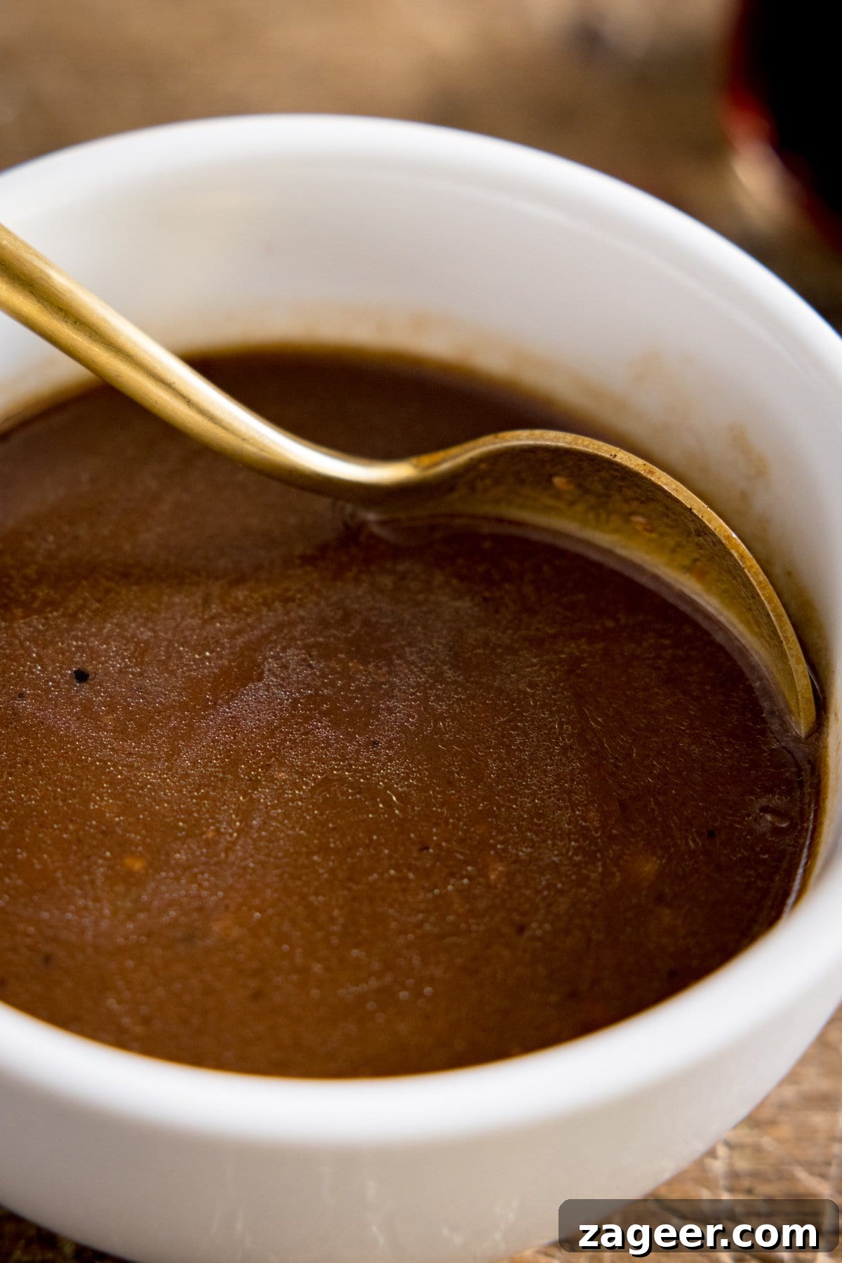 Rich Red Wine Jus Recipe for Steaks and Roasts 5 A white bowl of red wine jus being stirred with a spoon