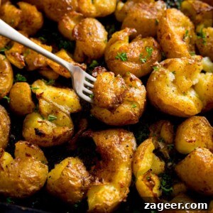 Crispy Garlic Smashed Potatoes Recipe for Perfectly Crispy Skins 7 A square photo of a tray of crispy smashed potatoes, with a fork with a smashed potato on the end