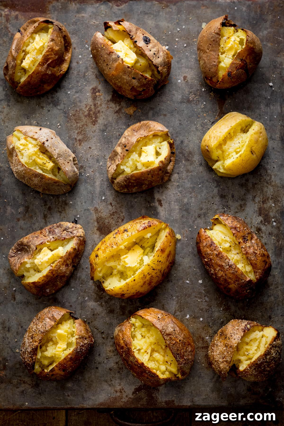 Perfect Baked Potato: Tips, Timing, and Crispy Skin Tricks 2 Tall overhead image showing 12 open baked potatoes on a metal tray