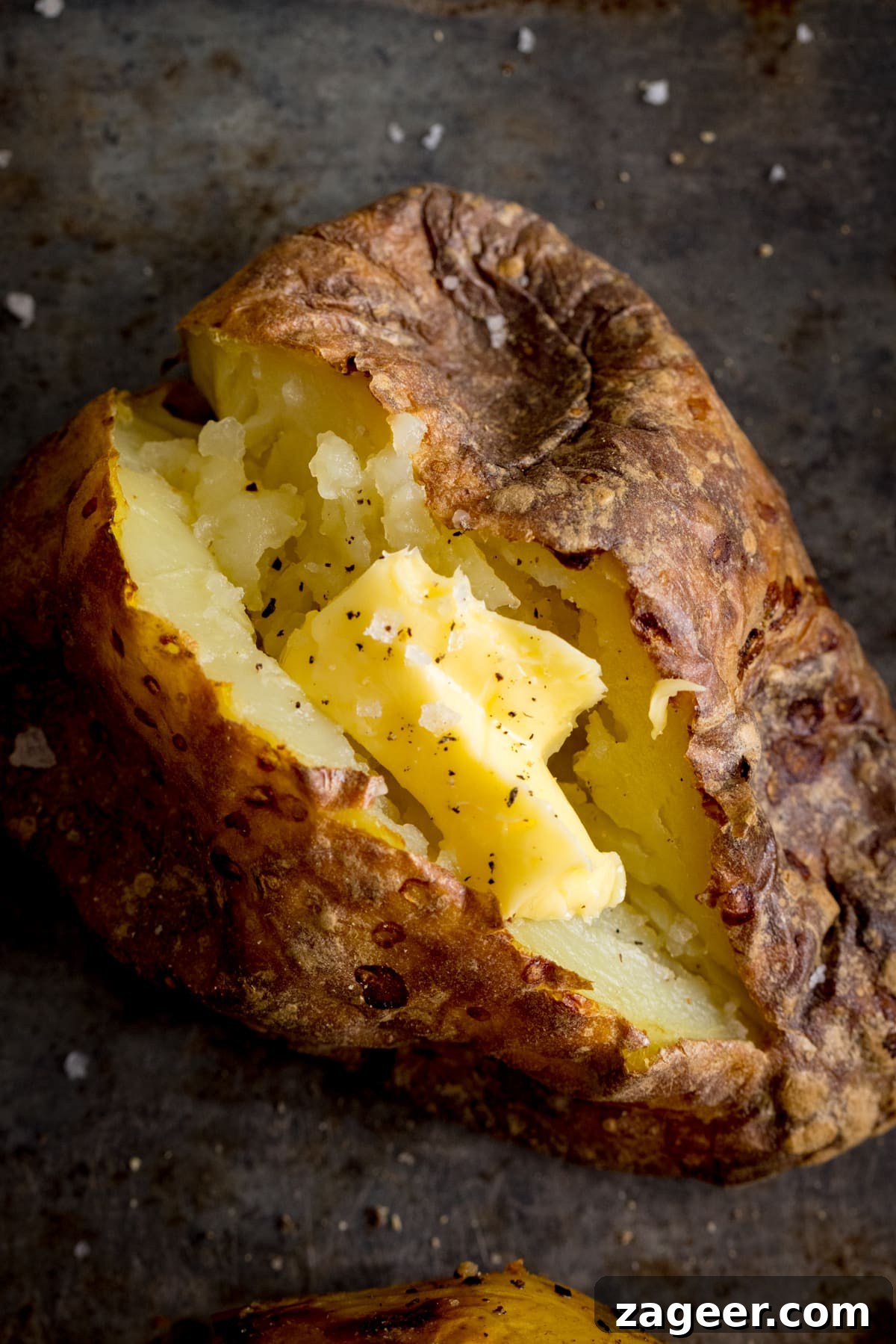 Perfect Baked Potato: Tips, Timing, and Crispy Skin Tricks 11 Overhead image of an open baked potato on a dark metal background. Potato was baked using method 7 of my baked potato experiment.
