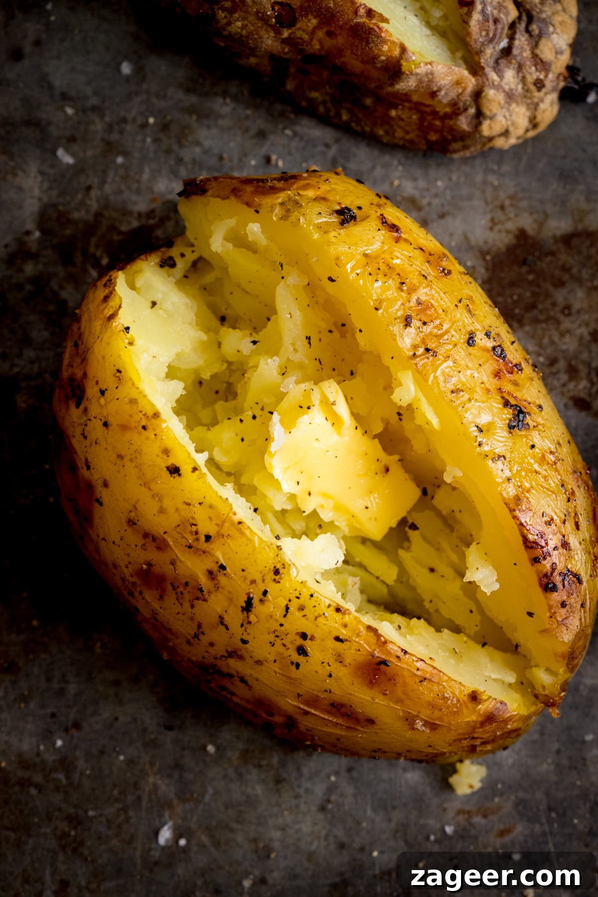 Perfect Baked Potato: Tips, Timing, and Crispy Skin Tricks 12 Overhead image of an open baked potato on a dark metal background. Potato was baked using method 8 of my baked potato experiment.