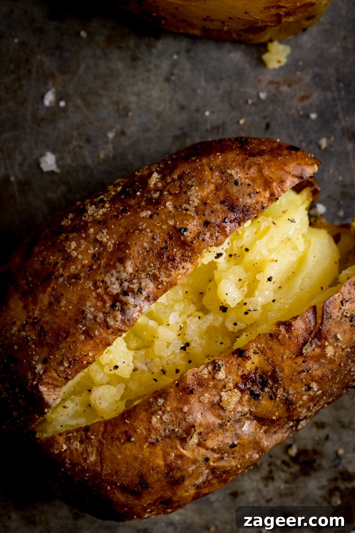 Perfect Baked Potato: Tips, Timing, and Crispy Skin Tricks 13 Overhead image of an open baked potato on a dark metal background. Potato was baked using method 9 of my baked potato experiment.