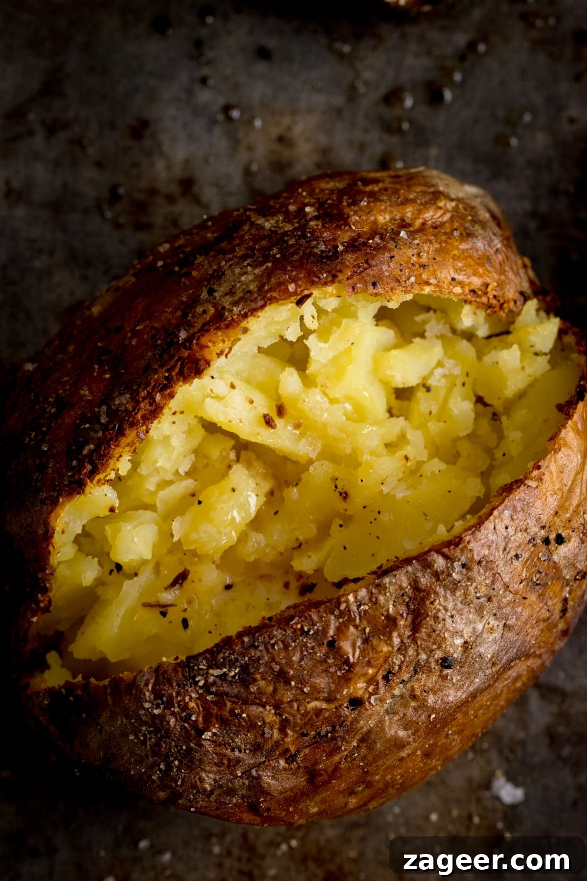 Perfect Baked Potato: Tips, Timing, and Crispy Skin Tricks 15 Overhead image of an open baked potato on a dark metal background. Potato was baked using method 11 of my baked potato experiment.