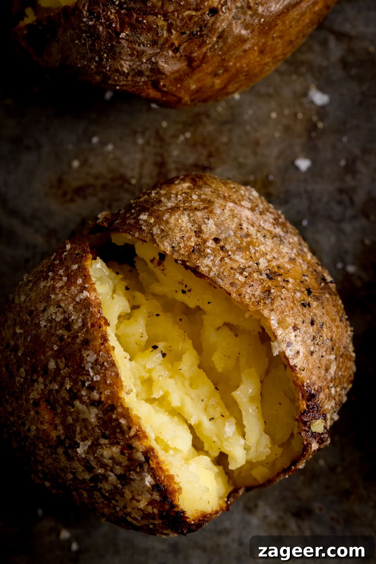 Perfect Baked Potato: Tips, Timing, and Crispy Skin Tricks 16 Overhead image of an open baked potato on a dark metal background. Potato was baked using method 12 of my baked potato experiment.