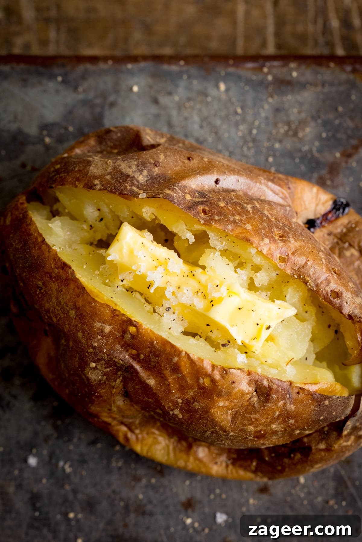 Perfect Baked Potato: Tips, Timing, and Crispy Skin Tricks 5 Overhead image of an open baked potato on a dark metal background. Potato was baked using method 1 of my baked potato experiment.