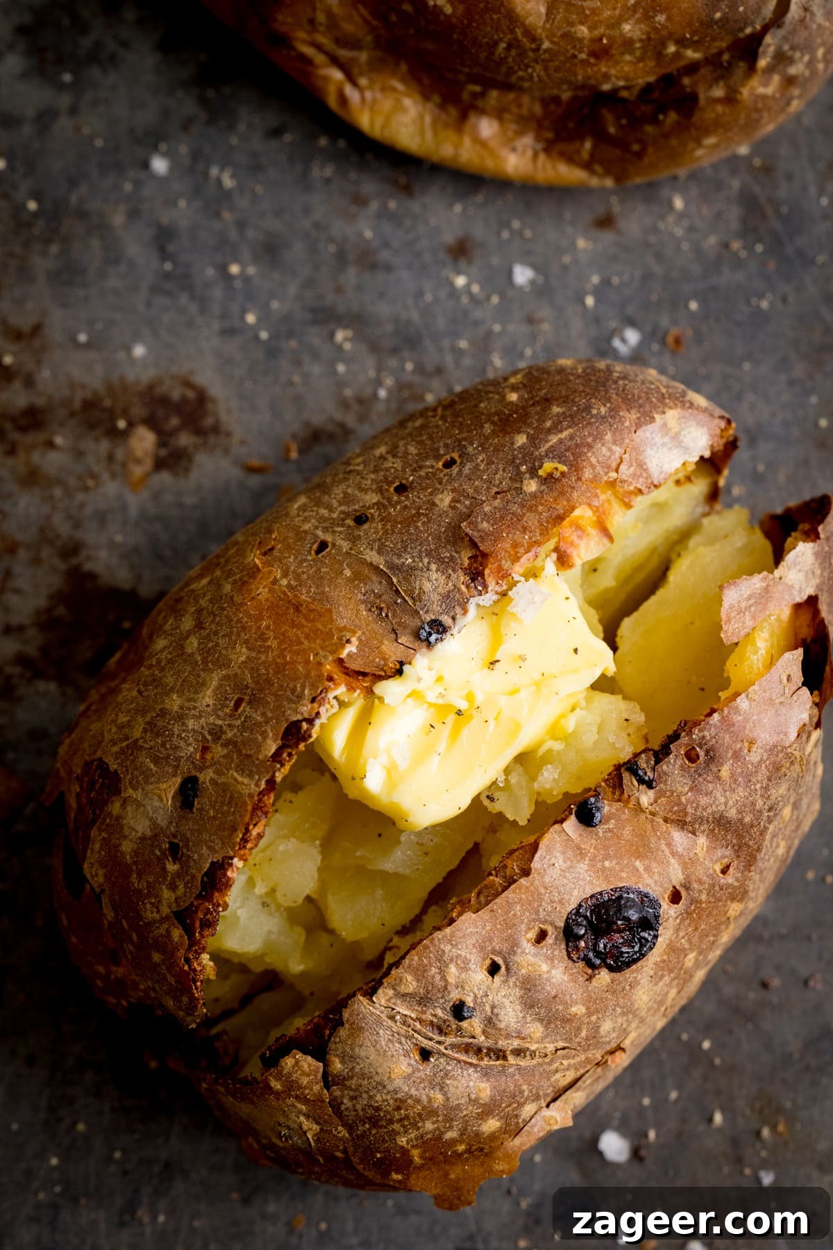 Perfect Baked Potato: Tips, Timing, and Crispy Skin Tricks 6 Overhead image of an open baked potato on a dark metal background. Potato was baked using method 2 of my baked potato experiment.