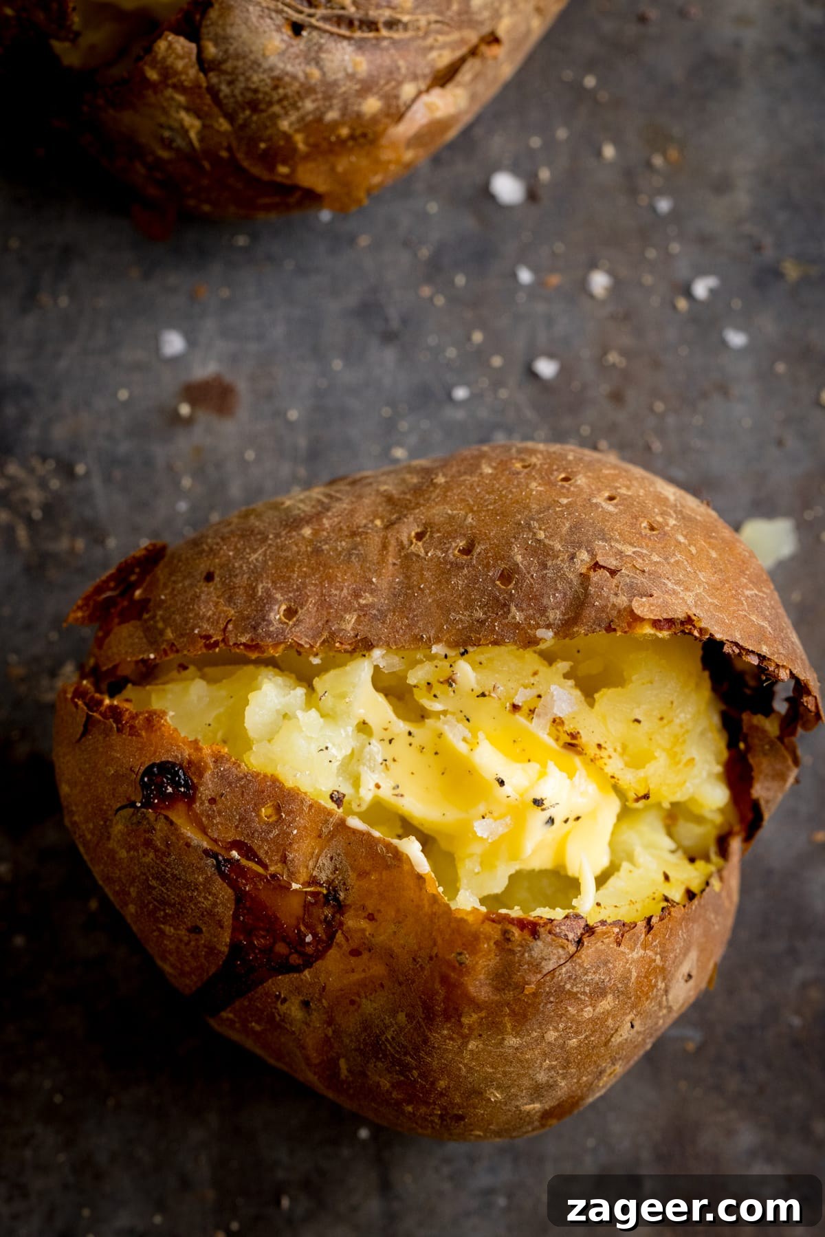 Perfect Baked Potato: Tips, Timing, and Crispy Skin Tricks 7 Overhead image of an open baked potato on a dark metal background. Potato was baked using method 3 of my baked potato experiment.