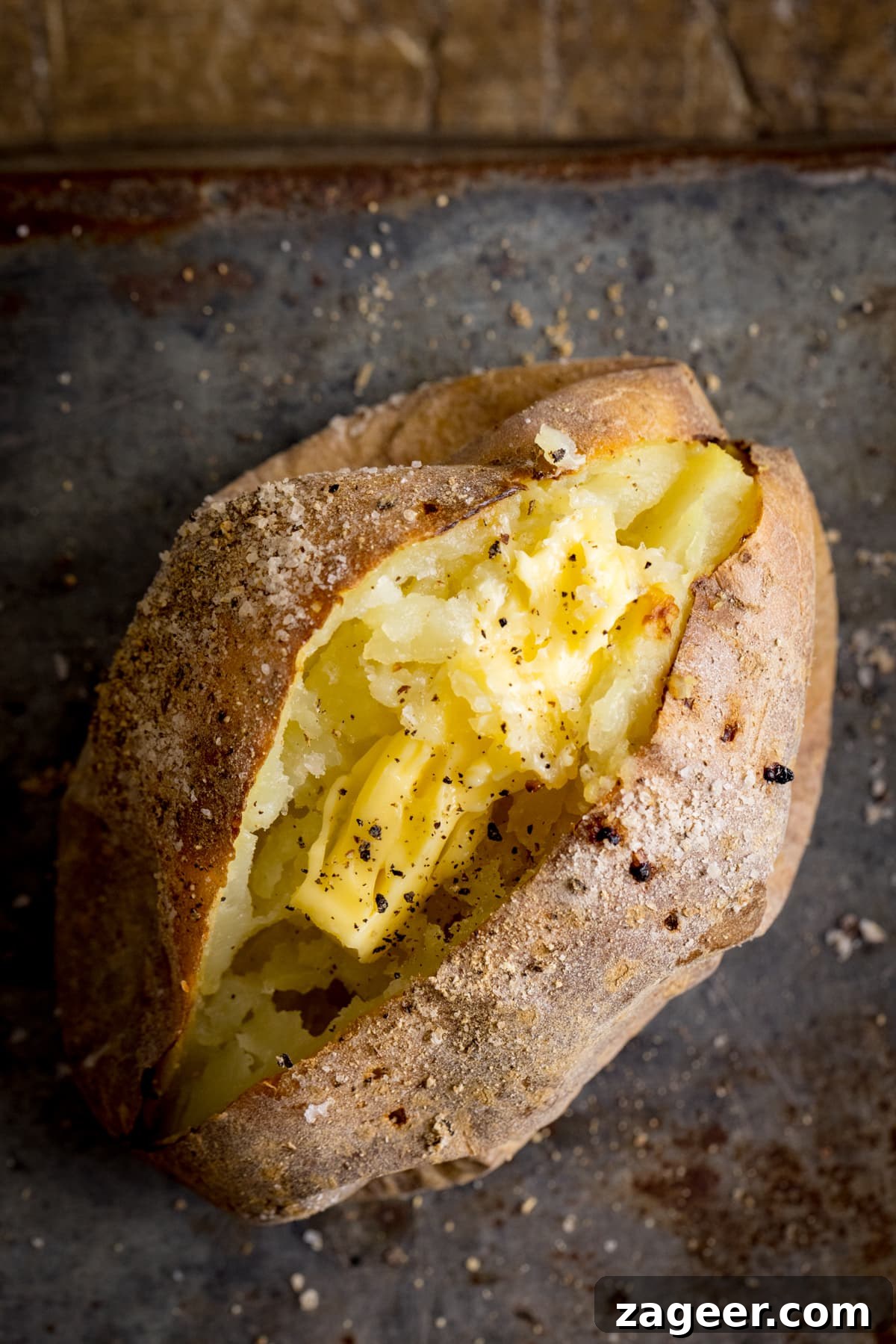 Perfect Baked Potato: Tips, Timing, and Crispy Skin Tricks 8 Overhead image of an open baked potato on a dark metal background. Potato was baked using method 4 of my baked potato experiment.