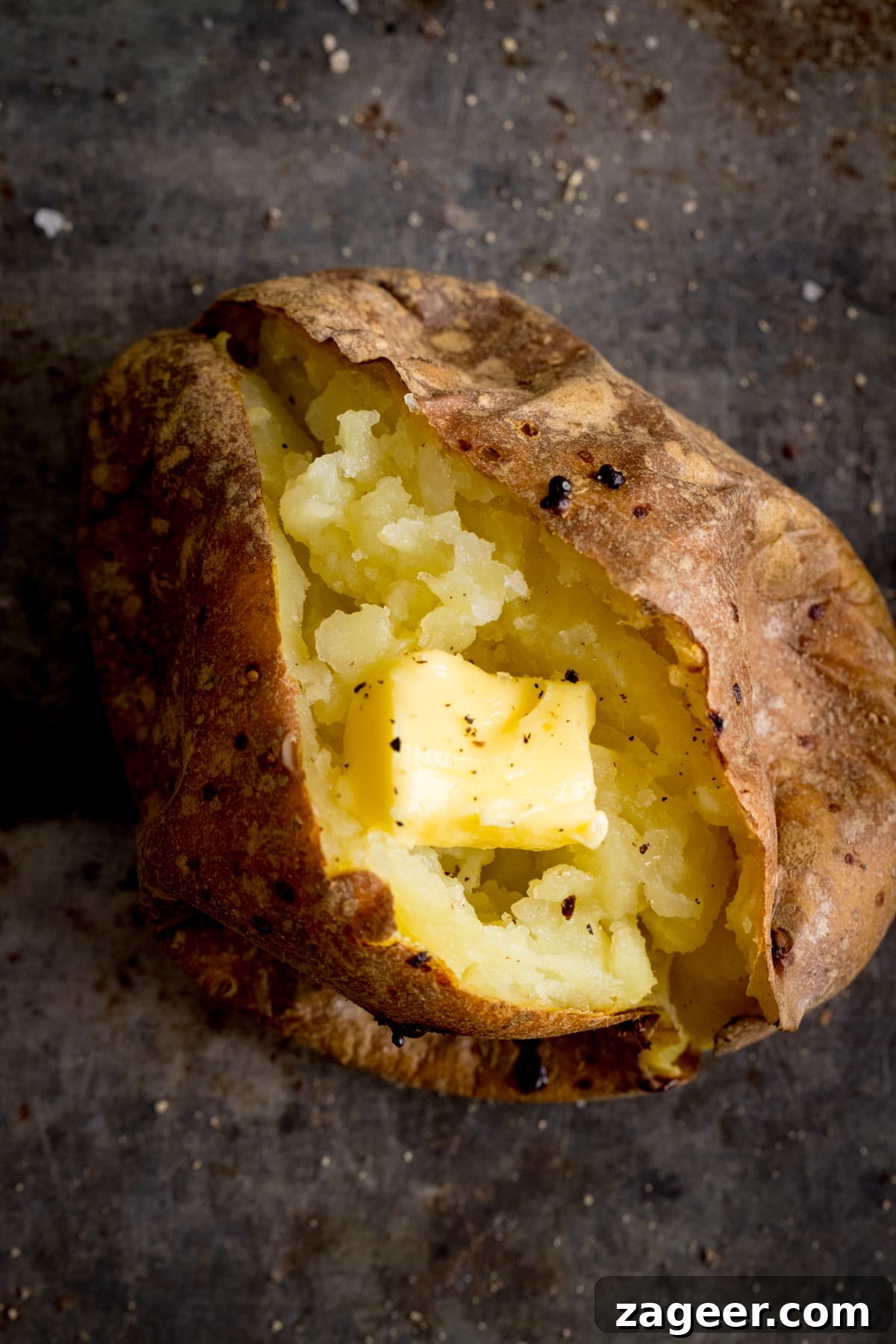 Perfect Baked Potato: Tips, Timing, and Crispy Skin Tricks 9 Overhead image of an open baked potato on a dark metal background. Potato was baked using method 5 of my baked potato experiment.