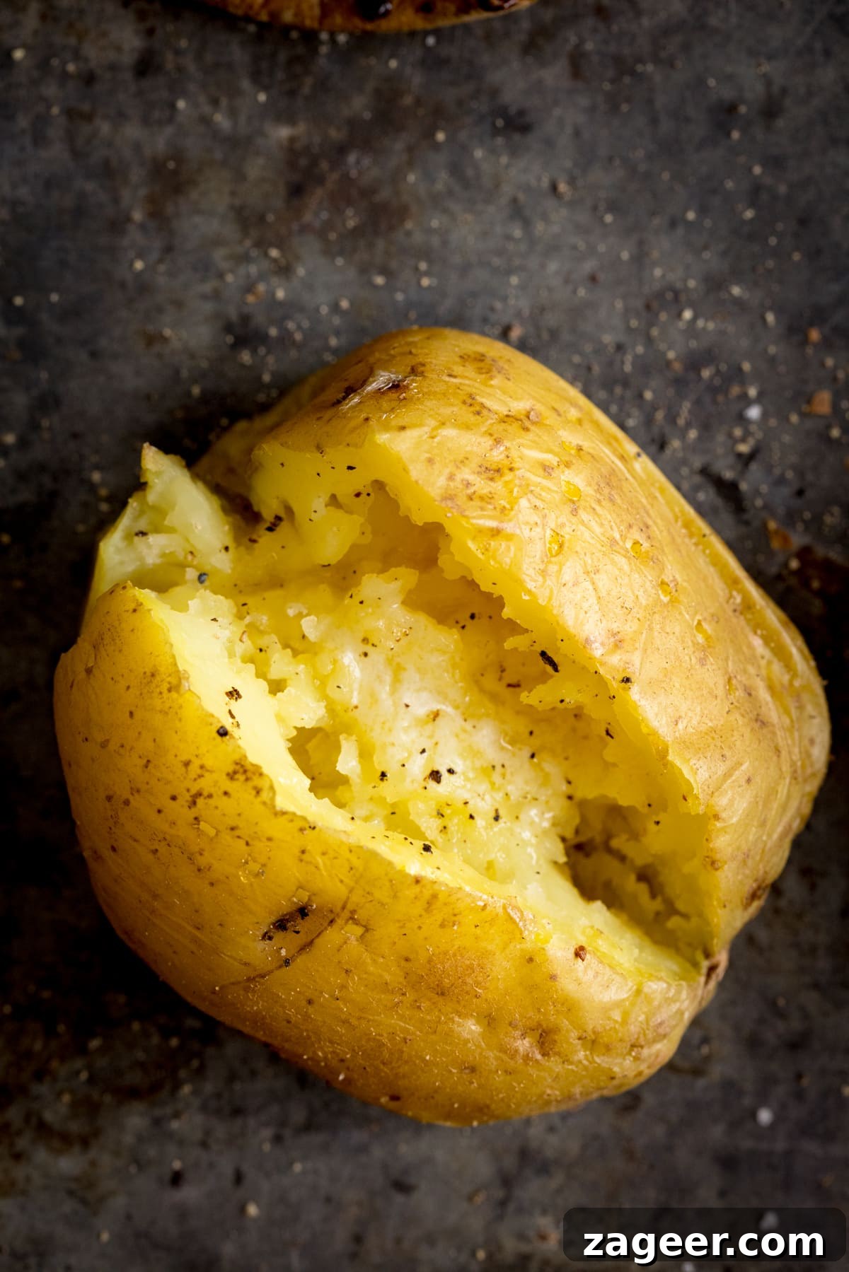 Perfect Baked Potato: Tips, Timing, and Crispy Skin Tricks 10 Overhead image of an open jacket potato on a dark metal background. Potato was cooked using method 6 of my baked potato experiment.