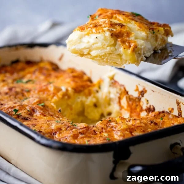 Perfectly Crispy Baked Potato: Foolproof Oven Method 7 A portion of cheesy potato dauphinoise is lifted from a rectangular baking tin, showing a golden, crispy top and creamy layers within.