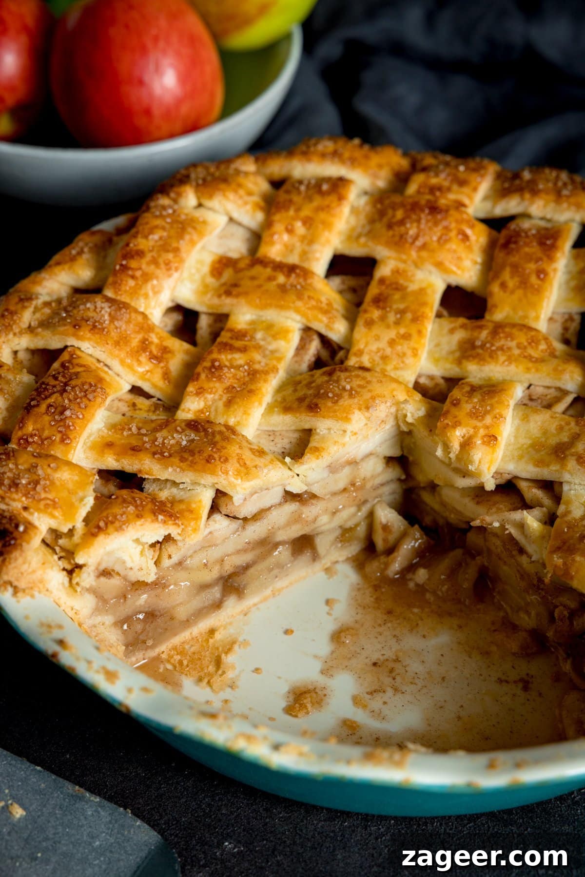 Ultimate Deep-Dish Apple Pie Recipe for Perfect Crust and Filling 5 A big round lattice topped deep dish apple pie cooked and golden brown with a wedge cut out of it, in a white tin