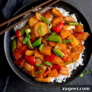 Sweet and Sour Vegetable Stir-Fry Recipe for Tangy Flavor 13 Square image of sweet and sour vegetables on a bed of boiled rice in a black bowl. There are chopsticks resting on the bowl.
