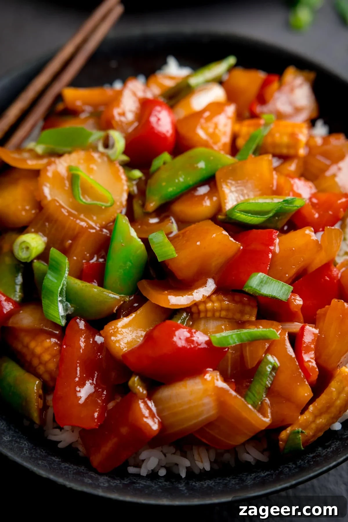 Sweet and Sour Vegetable Stir-Fry Recipe for Tangy Flavor 6 Close up of sweet and sour vegetables in a dark bowl. A pair of chopsticks is just in shot, resting on the bowl.