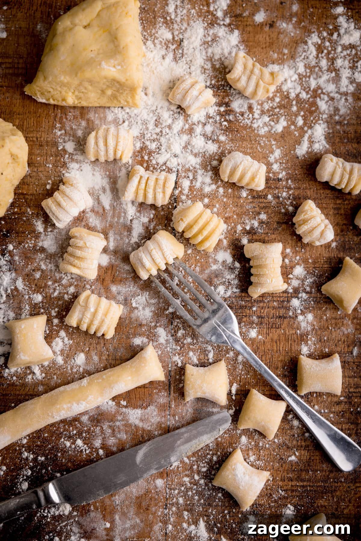 Authentic Homemade Potato Gnocchi Recipe for Fluffy Results 2 Tall image of Gnocchi being cut and shaped on a wooden board. There is a fork in shot - used for rolling into a ridged shape.