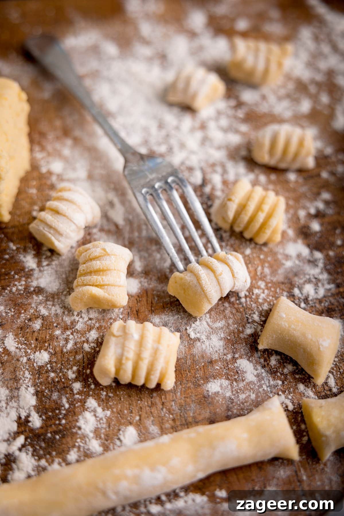 Authentic Homemade Potato Gnocchi Recipe for Fluffy Results 5 Gnocchi being shaped using the back of a fork on a floured board. There are pieces of gnocchi around the fork.
