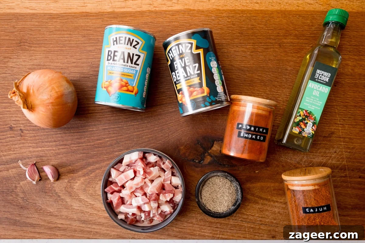 Smoky Barbecue Baked Beans Recipe for Summer Cookouts 3 An overhead shot of the ingredients for Easy BBQ Beans. The ingredients are laid out on a wooden cutting board. They are as follows: an onion, 2 cloves of garlic, beans in tomato sauce, 5 means in tomato sauce, bacon lardons, smoked paprika, ground black pepper, avocado oil and cajun seasoning.