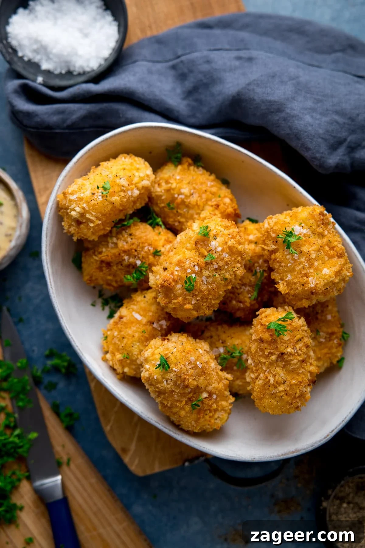 Cheesy Baked Potato Croquettes: Crispy Oven-Baked Recipe 2 potato croquettes in a white bowl on a wooden board next to a blue napkin