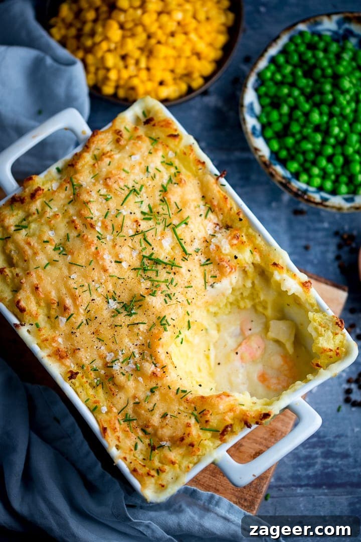 Fish pie with mashed potato on a blue background. Peas and corn in background.