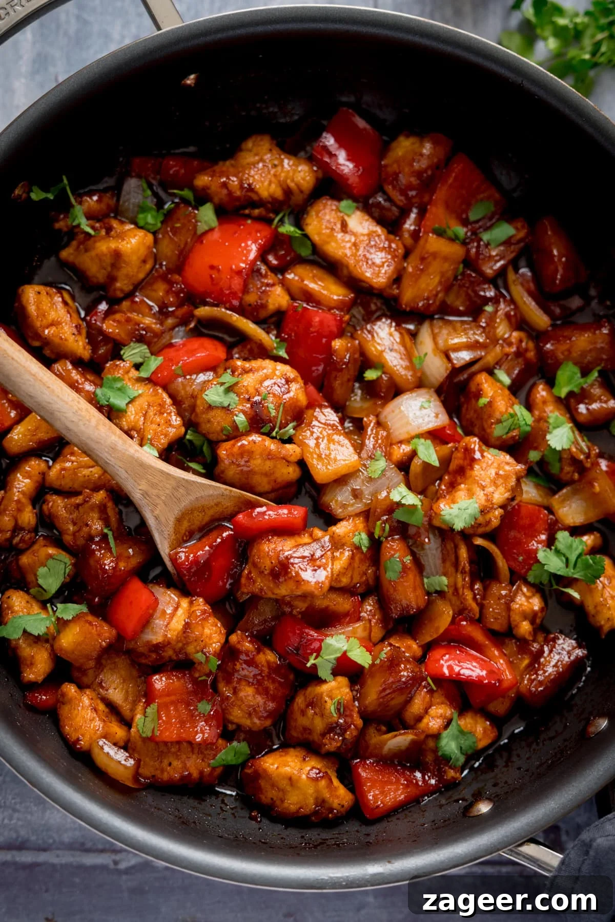 Sticky Pineapple Chicken Recipe with Sweet Tangy Glaze 2 Tall overhead image of Sticky Pineapple Chicken Stir Fry in a pan. There is a wooden spoon sticking out of the pan.