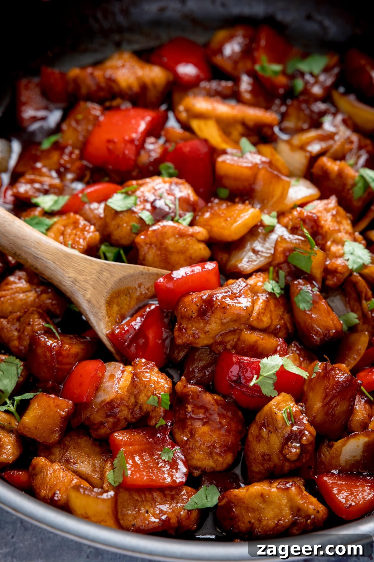 Sticky Pineapple Chicken Recipe with Sweet Tangy Glaze 4 Close up of Sticky Pineapple Chicken Stir Fry in a pan, with a wooden spoon being used to stir the chicken.