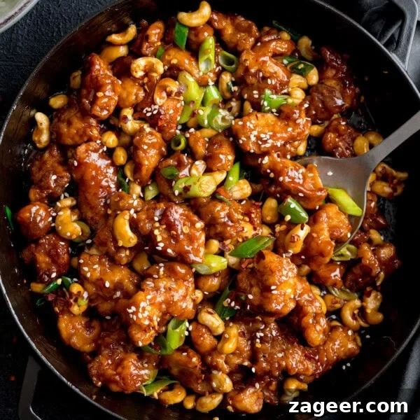 Crispy Chicken Skin Cracklings with Savory Butter Dip 11 A pan filled with Cashew Chicken in a glossy brown sauce, garnished with sliced spring onions and sesame seeds, with a serving spoon on the side.